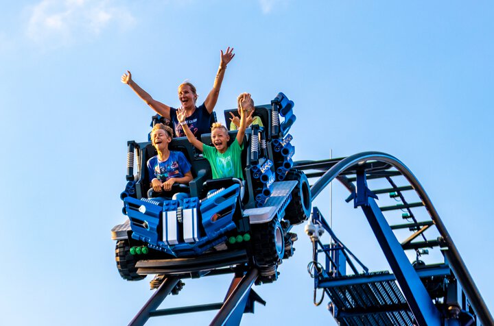Frau mit dreii Kindern auf einem bauen Achterbahnwaggon, der bergab fährt  | © Canva 